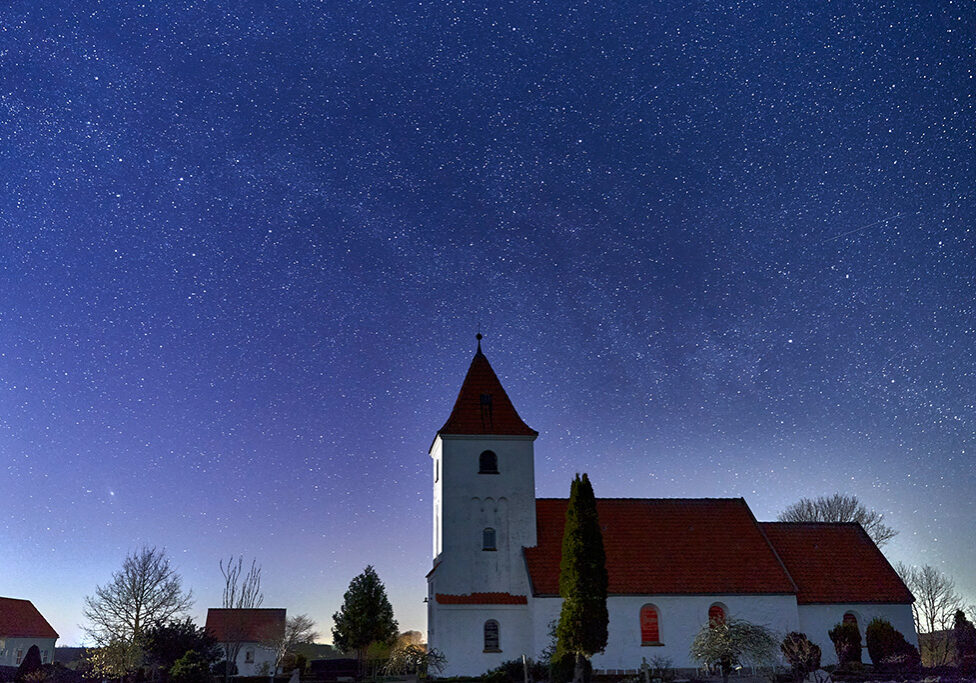 En hvid dansk kirke, Vester kirke, under en mørke blå stjernehimmel