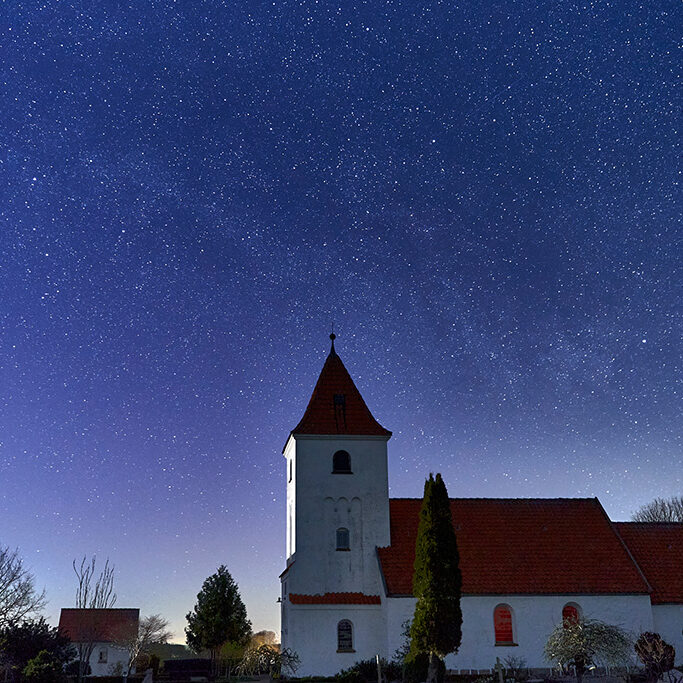 En hvid dansk kirke, Vester kirke, under en mørke blå stjernehimmel